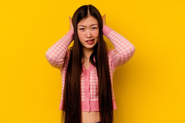 Jeune femme chinoise isolée sur un mur jaune couvrant les oreilles avec les mains en essayant de ne pas entendre un son trop fort