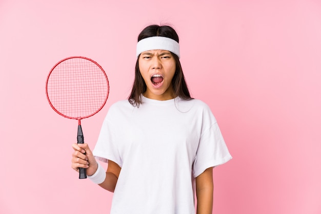 Jeune femme chinoise jouant au badminton dans un mur rose criant très en colère et agressif.