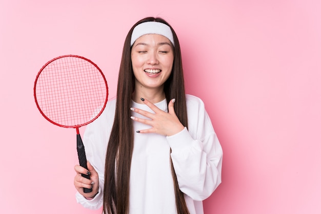 Jeune femme chinoise jouant au badminton isolé rit à haute voix en gardant la main sur la poitrine.