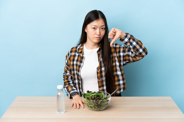 Jeune femme chinoise mangeant une salade montrant le pouce vers le bas avec une expression négative