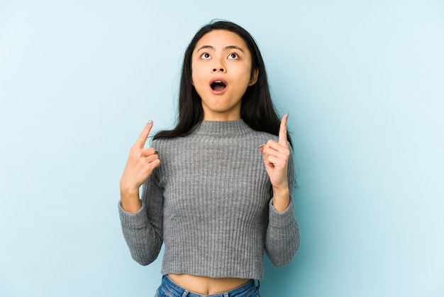 Jeune femme chinoise sur un mur bleu pointant à l'envers avec la bouche ouverte.