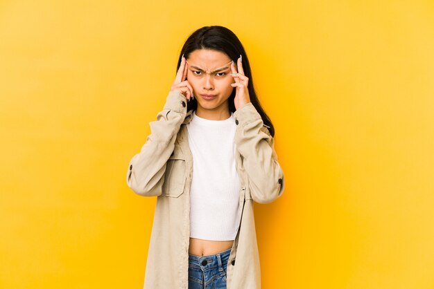 Jeune femme chinoise sur un mur jaune concentré sur une tâche, gardant les index pointant la tête.