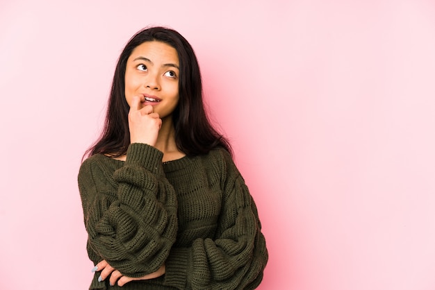 Jeune femme chinoise sur un mur rose détendu penser à quelque chose en regardant un espace vide.