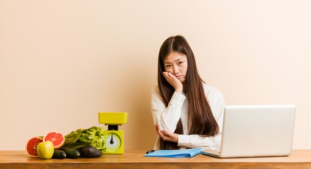 Jeune femme chinoise nutritionniste travaillant avec son ordinateur portable qui s'ennuie, est fatiguée et a besoin d'une journée de détente.