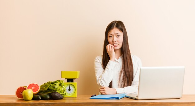 Jeune femme chinoise nutritionniste travaillant avec son ordinateur portable se ronger les ongles, nerveuse et très anxieuse.