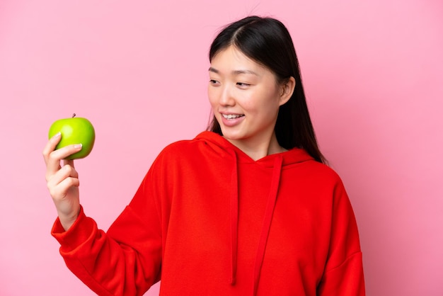 Jeune femme chinoise avec une pomme isolée sur fond rose avec une expression heureuse