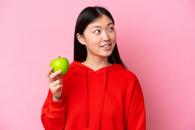 Jeune femme chinoise avec une pomme isolée sur fond rose levant les yeux en souriant