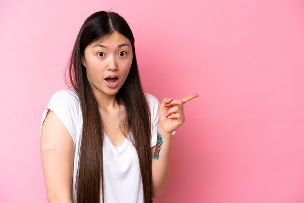 Jeune femme chinoise portant un pansement isolé sur fond rose surpris et pointant du côté