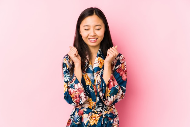 Jeune femme chinoise portant un pyjama kimono isolé levant le poing, se sentant heureux et réussi. Concept de victoire.