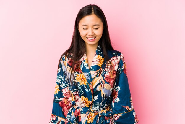 Photo jeune femme chinoise portant un pyjama kimono isolé rit et ferme les yeux, se sent détendue et heureuse.