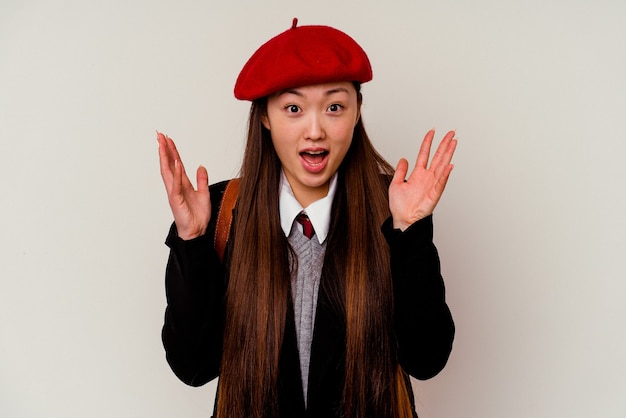 Jeune femme chinoise portant un uniforme scolaire isolé sur un mur blanc recevant une agréable surprise, excitée et levant les mains