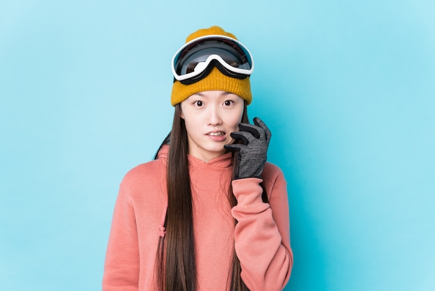 Jeune femme chinoise portant des vêtements de ski isolés se rongeant les ongles, nerveux et très anxieux.