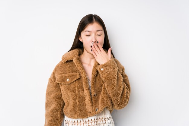 Jeune femme chinoise posant dans un mur blanc bâillant montrant un geste fatigué couvrant la bouche avec la main.