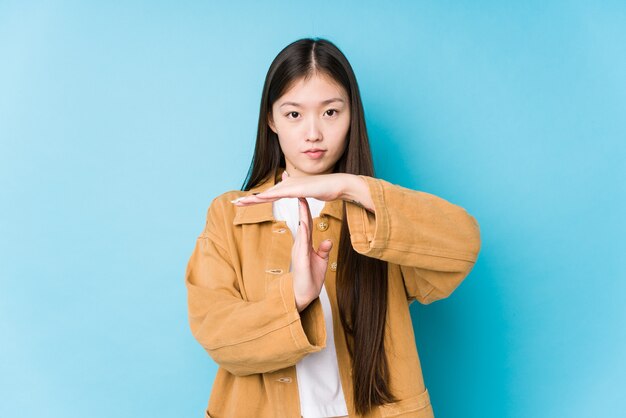 Jeune femme chinoise posant dans un mur bleu isolé montrant un geste de temporisation.