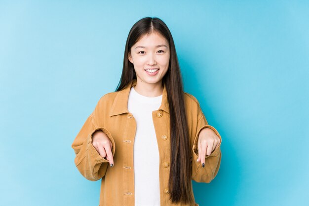 Jeune femme chinoise posant dans un mur bleu isolé pointe vers le bas avec les doigts, sentiment positif.