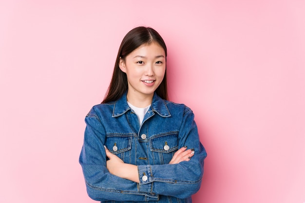 Jeune femme chinoise posant dans un mur rose isolé qui se sent confiant, croisant les bras avec détermination.