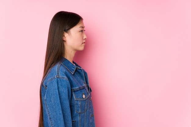 Jeune femme chinoise posant dans un mur rose isolé regardant à gauche, pose sur le côté.