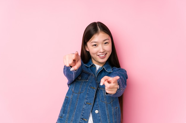 Jeune femme chinoise posant dans un mur rose isolé sourires joyeux pointant vers l'avant.