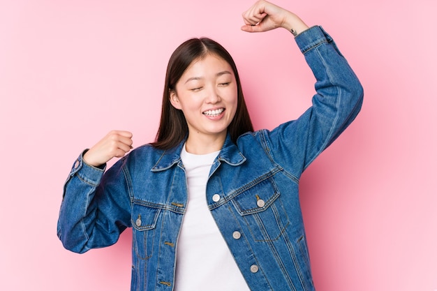 Jeune femme chinoise posant sur rose isolé célébrant une journée spéciale, saute et lève les bras avec énergie.