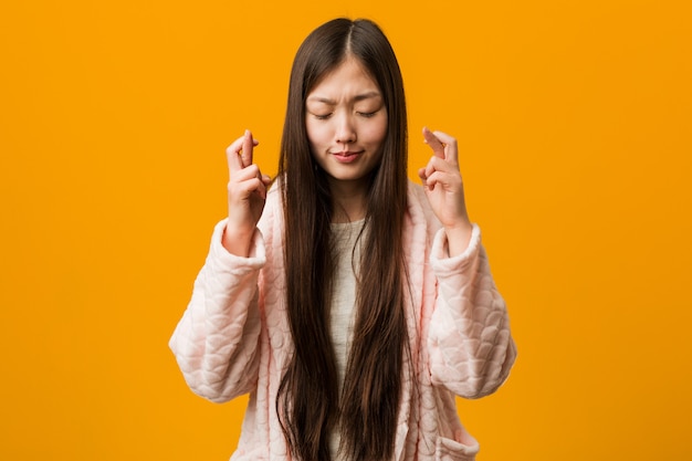 Jeune femme chinoise en pyjama croise les doigts pour avoir de la chance