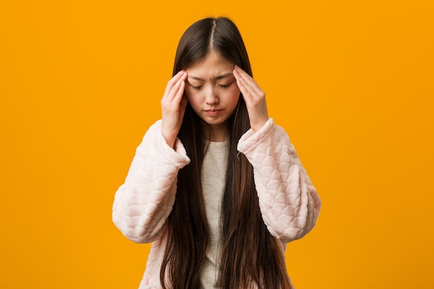 Jeune femme chinoise en pyjama touchant les tempes et ayant mal à la tête.