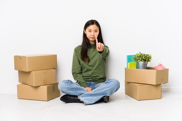 Jeune femme chinoise se déplaçant vers une nouvelle maison montrant le numéro un avec le doigt.