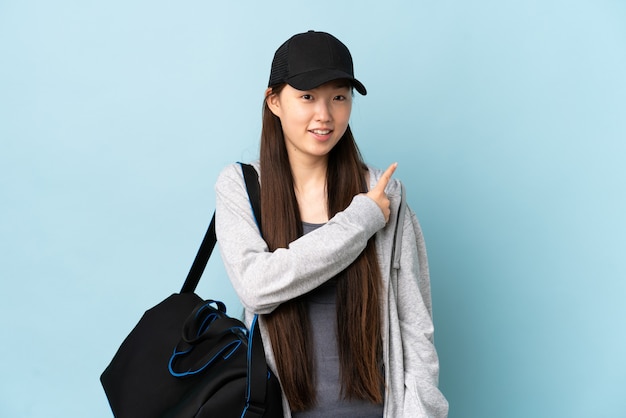 Jeune femme chinoise de sport avec sac de sport sur le côté bleu surpris et pointant