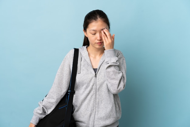 Jeune femme chinoise de sport avec sac de sport sur mur bleu isolé avec maux de tête