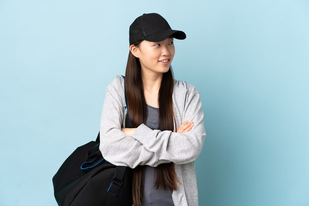 Jeune femme chinoise de sport avec sac de sport sur mur bleu isolé en regardant tout en souriant