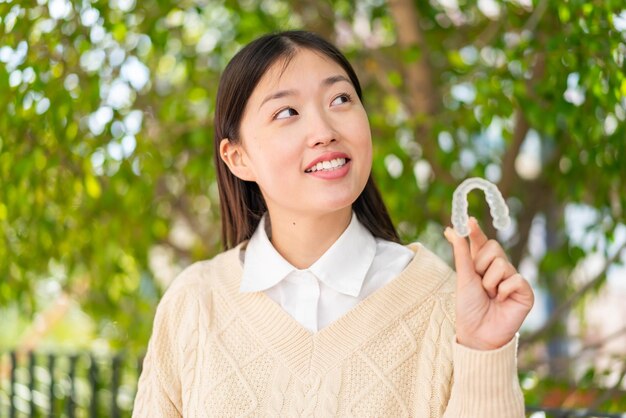 Jeune femme chinoise tenant des accolades invisibles à l'extérieur en levant les yeux tout en souriant