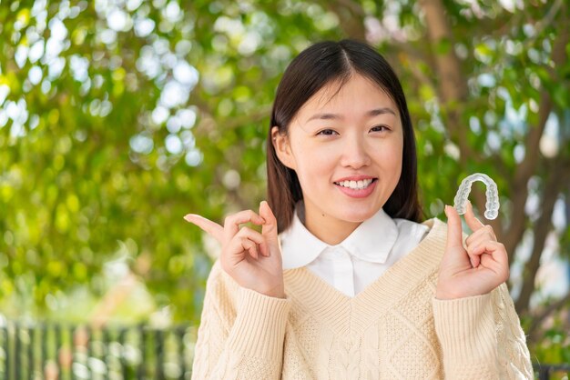 Jeune femme chinoise tenant des accolades invisibles à l'extérieur surpris et pointant le doigt sur le côté