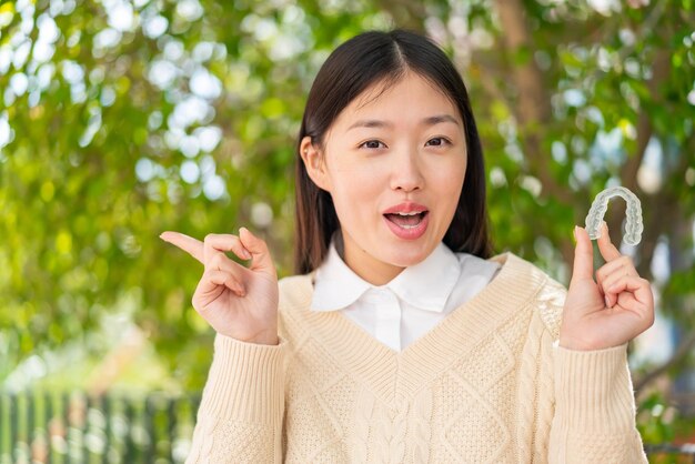 Jeune femme chinoise tenant des accolades invisibles à l'extérieur surpris et pointant du côté