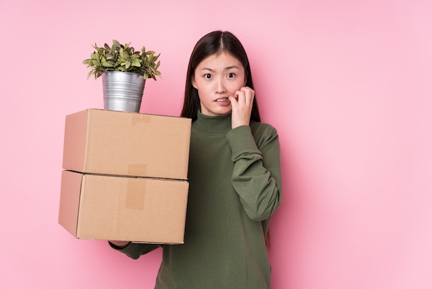 Jeune femme chinoise tenant des boîtes isolées se rongeant les ongles, nerveuse et très anxieuse.