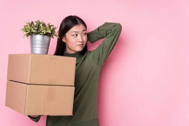 Jeune femme chinoise tenant des boîtes isolées touchant l'arrière de la tête, pensant et faisant un choix.