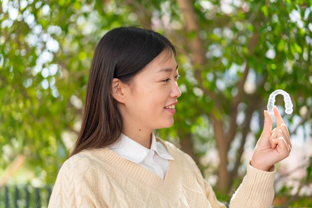 Jeune femme chinoise tenant des bretelles invisibles à l'extérieur avec une expression heureuse