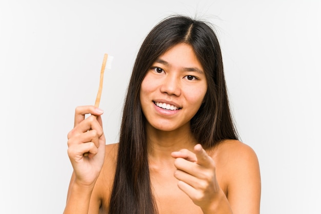 Jeune femme chinoise tenant une brosse à dents sourires joyeux isolés pointant vers l'avant.