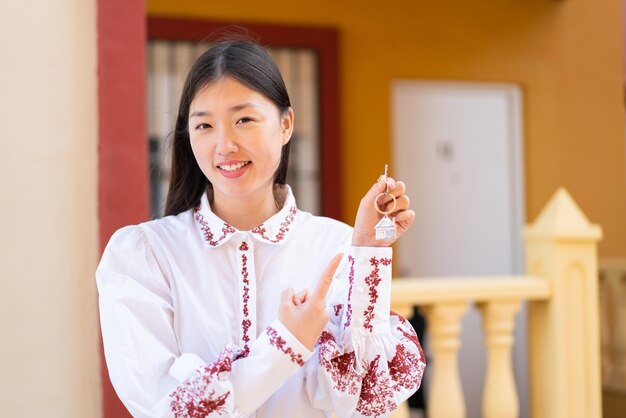 Jeune femme chinoise tenant les clés de la maison à l'extérieur et le pointant