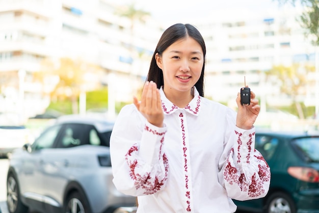 Jeune femme chinoise tenant des clés de voiture à l'extérieur invitant à venir avec la main Heureux que vous soyez venu