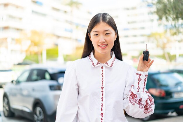 Jeune femme chinoise tenant des clés de voiture à l'extérieur souriant beaucoup