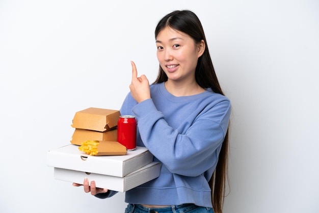 Jeune femme chinoise tenant fast food isolé sur fond blanc pointant vers l'arrière