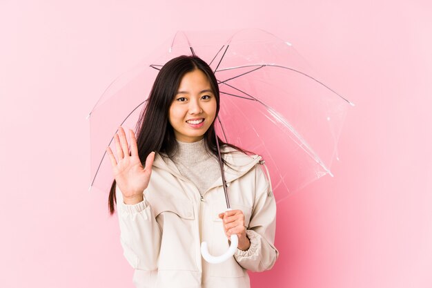 Jeune femme chinoise tenant un parapluie isolé souriant joyeux montrant le numéro cinq avec les doigts.