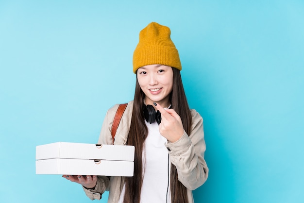 Jeune femme chinoise tenant des pizzas isolées pointant du doigt vers vous comme si vous vous invitiez à vous rapprocher.