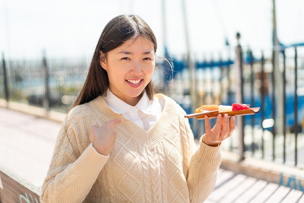 Jeune femme chinoise tenant des sashimis à l'extérieur avec une expression faciale surprise