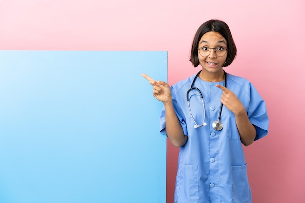 Jeune femme chirurgien métisse avec une grande bannière sur fond isolé effrayé et pointant vers le côté