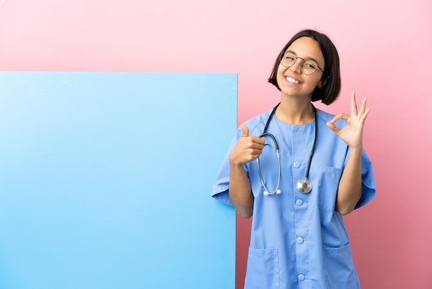 Jeune femme chirurgien métisse avec une grande bannière fond isolé montrant un signe ok et un geste du pouce vers le haut