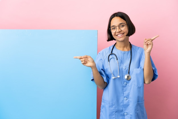 Jeune femme chirurgien métisse avec une grande bannière sur fond isolé, pointant le doigt vers les latéraux et heureux