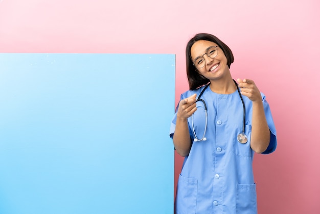 Jeune femme de chirurgien métisse avec une grande bannière sur fond isolé pointant vers l'avant avec une expression heureuse