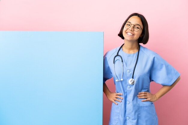 Jeune femme chirurgien métisse avec une grande bannière sur fond isolé posant avec les bras à la hanche et souriant