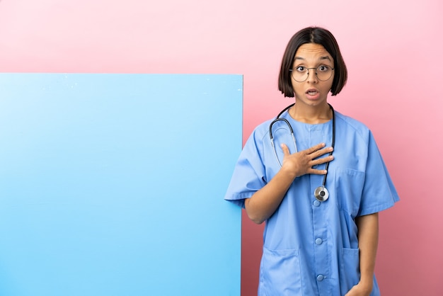 Jeune femme chirurgien métisse avec une grande bannière sur fond isolé surpris et choqué en regardant à droite