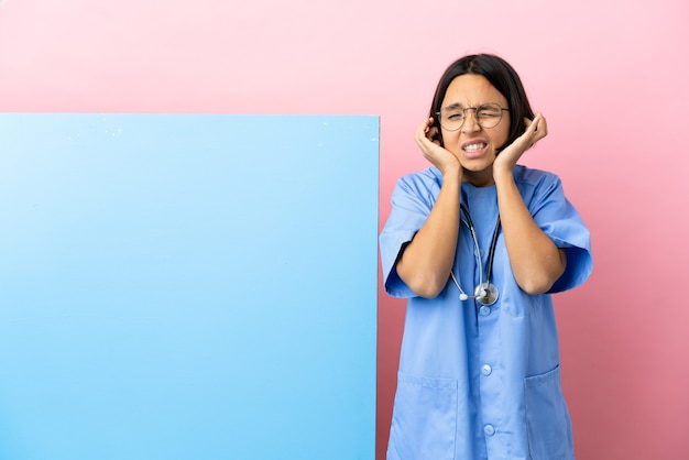 Jeune femme chirurgien métisse avec une grande bannière isolé sur fond frustré et couvrant les oreilles